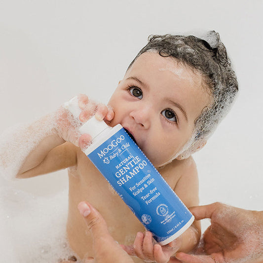 baby in bath with shampoo foam on scalp and holding MooGoo Gentle Shampoo, natural tear-free formula for delicate newborn and child skin