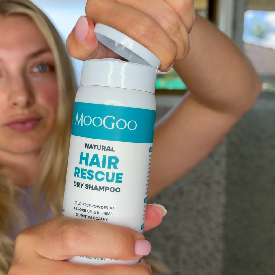 Woman Holding a turquoise and white bottle of MooGoo Hair Rescue Dry Shampoo with the lid open. Natural talc free formula. Adds volume and texture without aerosols. 
