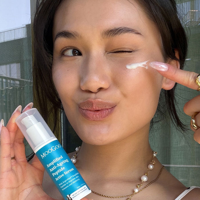 Woman with glowing, plump skin applying MooGoo Amplified Argireline Serum to her face.