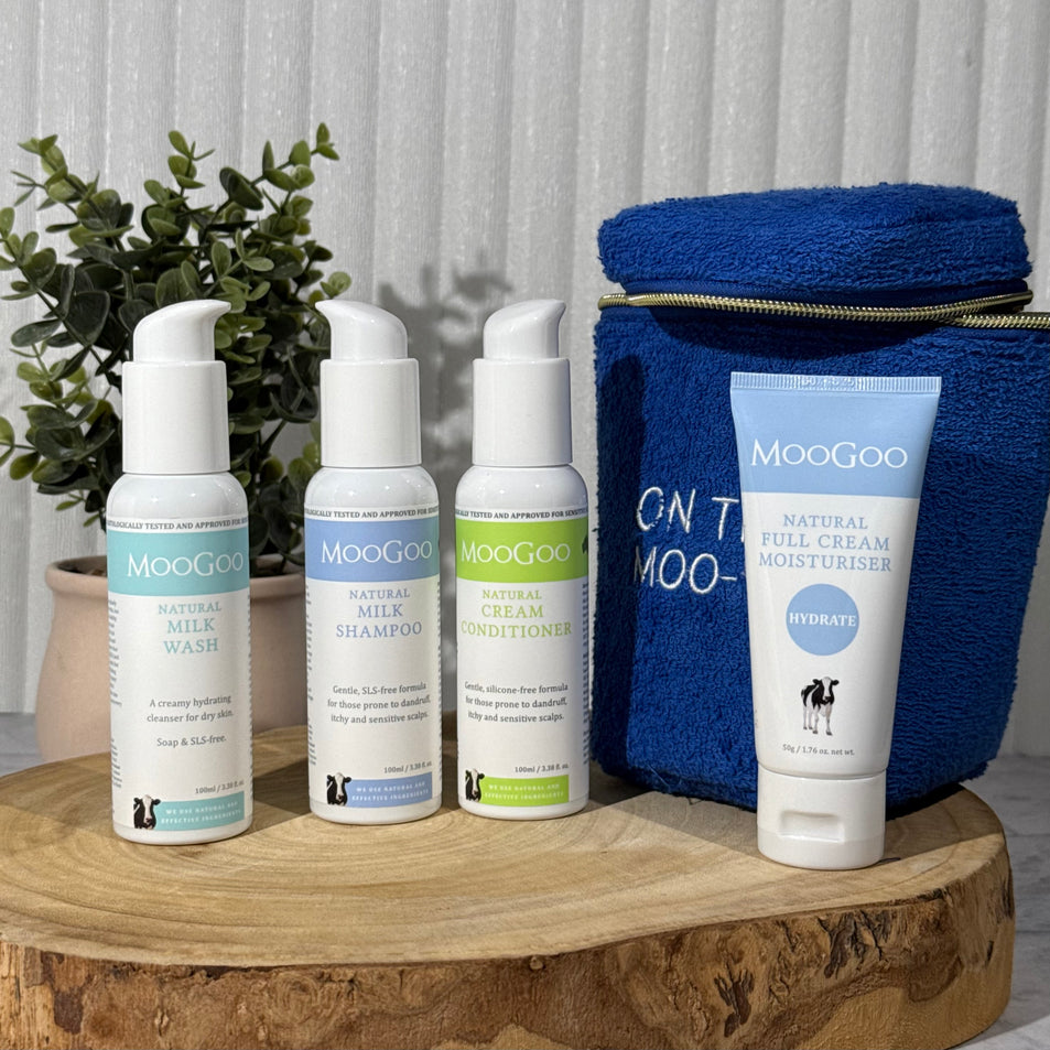 MooGoo Travel Pack on a wooden board with a plant in the background, including travel-sized Milk Shampoo, Cream Conditioner, Milk Wash and Full Cream Moisturizer - ideal for sensitive skin, hydration and scalp health