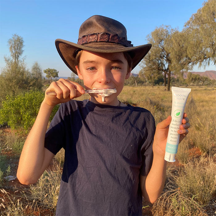 Young boy brushing teeth outdoors holding MooGoo Natural Moothpaste, natural fluoride-free toothpaste for kids and adults with hydroxyapatite